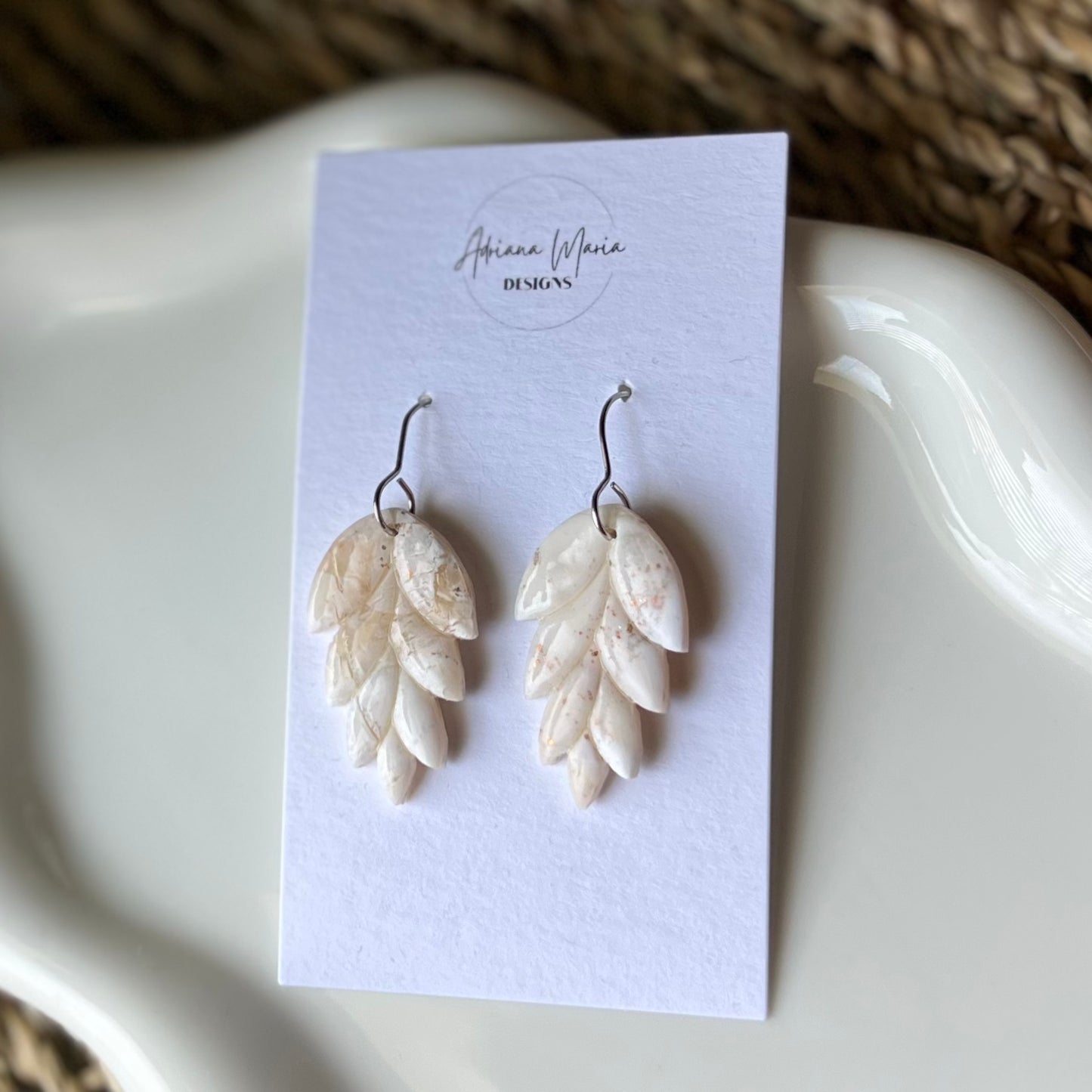Pair of leaf-shaped earrings on a card with 'Arianna Maria Designs' branding, displayed on a white surface.