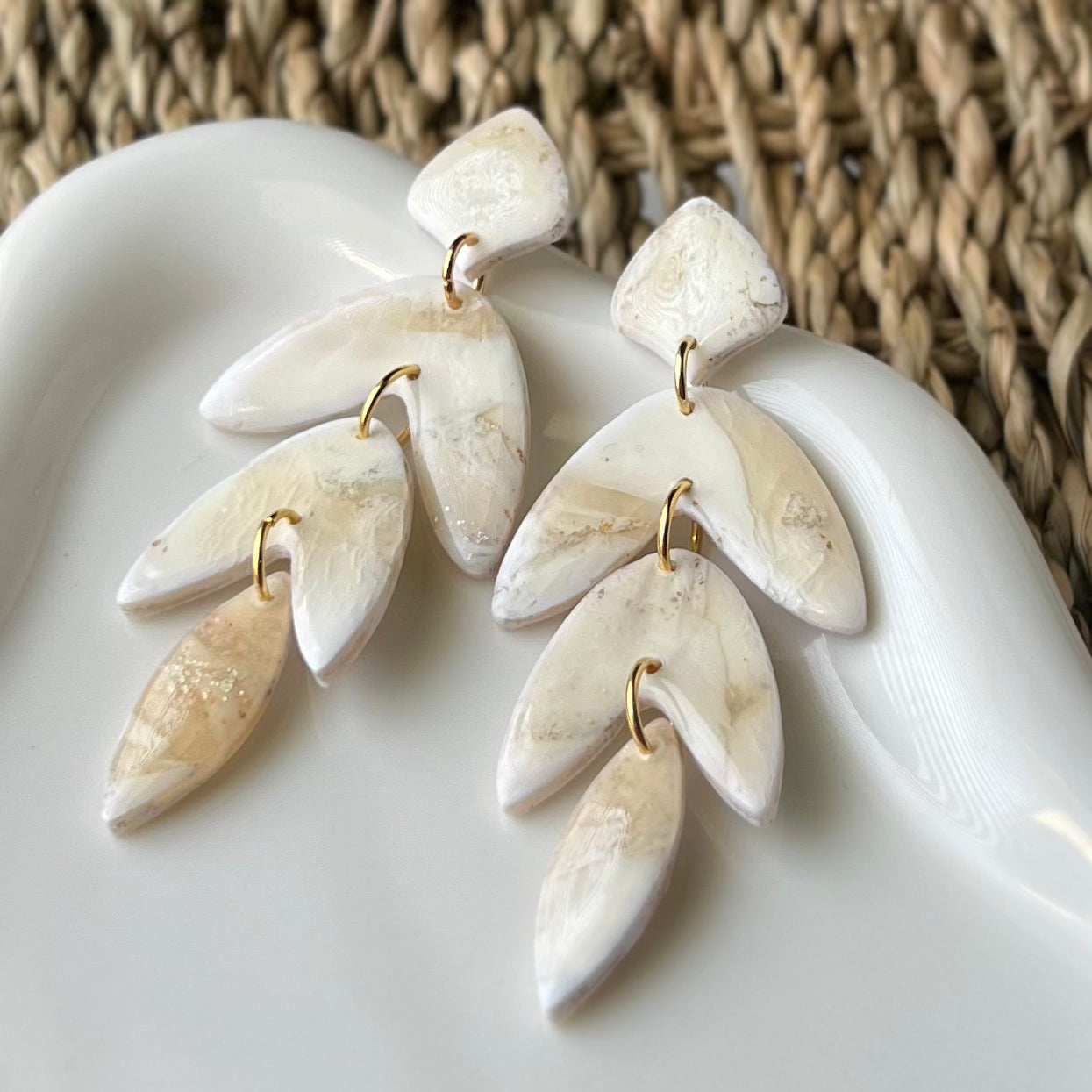 White marbled leaf-shaped earrings on a white surface with a woven background
