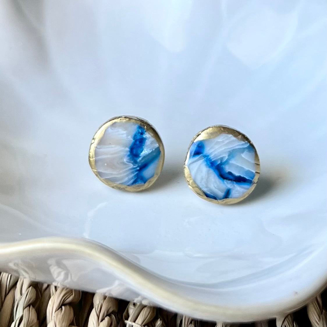 Round earrings with blue and white marbled design on a white dish.