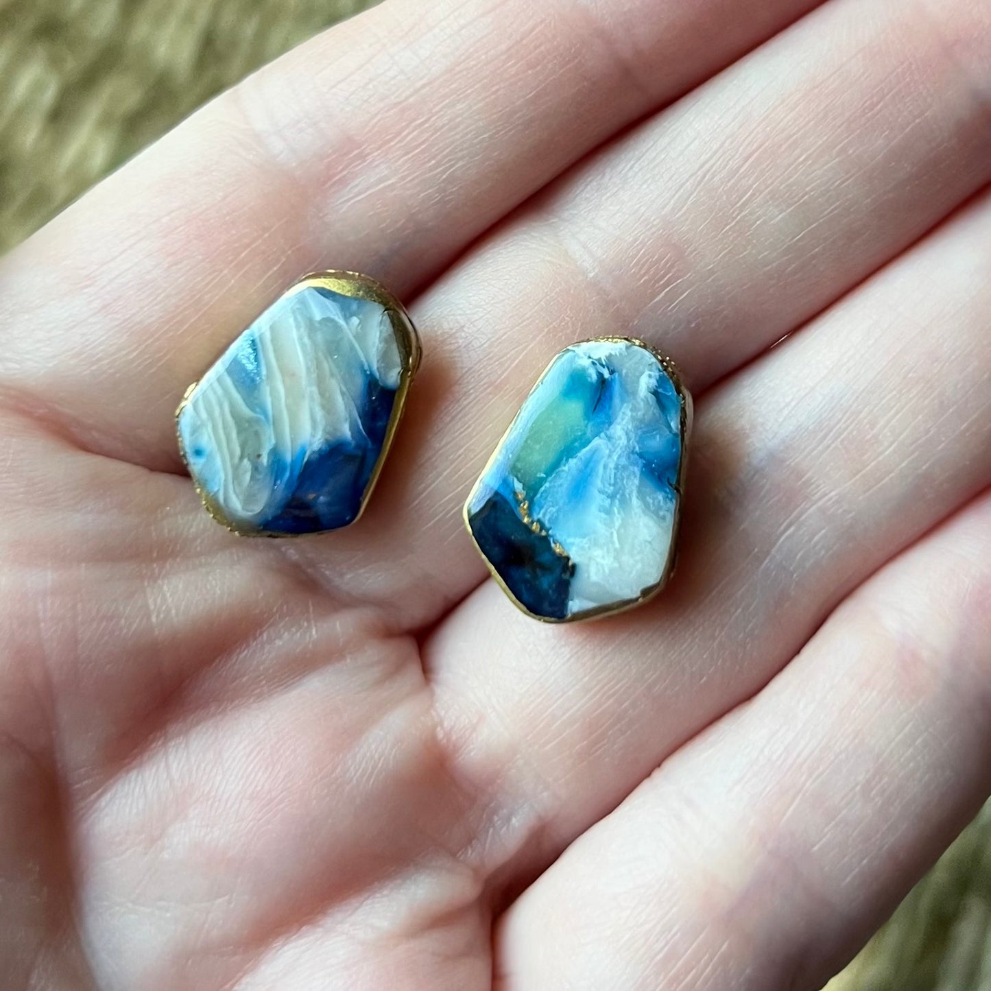Two blue marbled earrings held between fingers