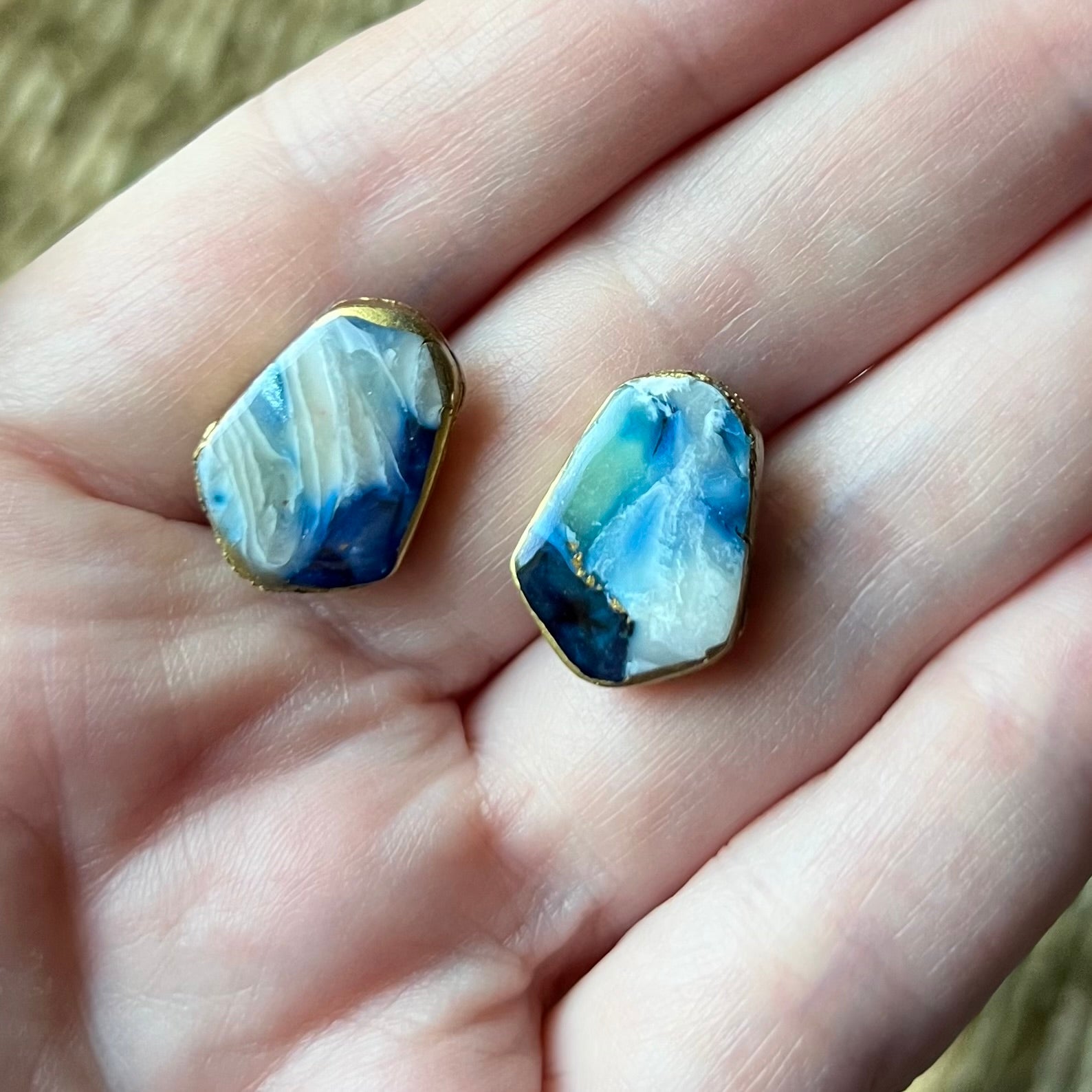 Two blue marbled earrings held between fingers