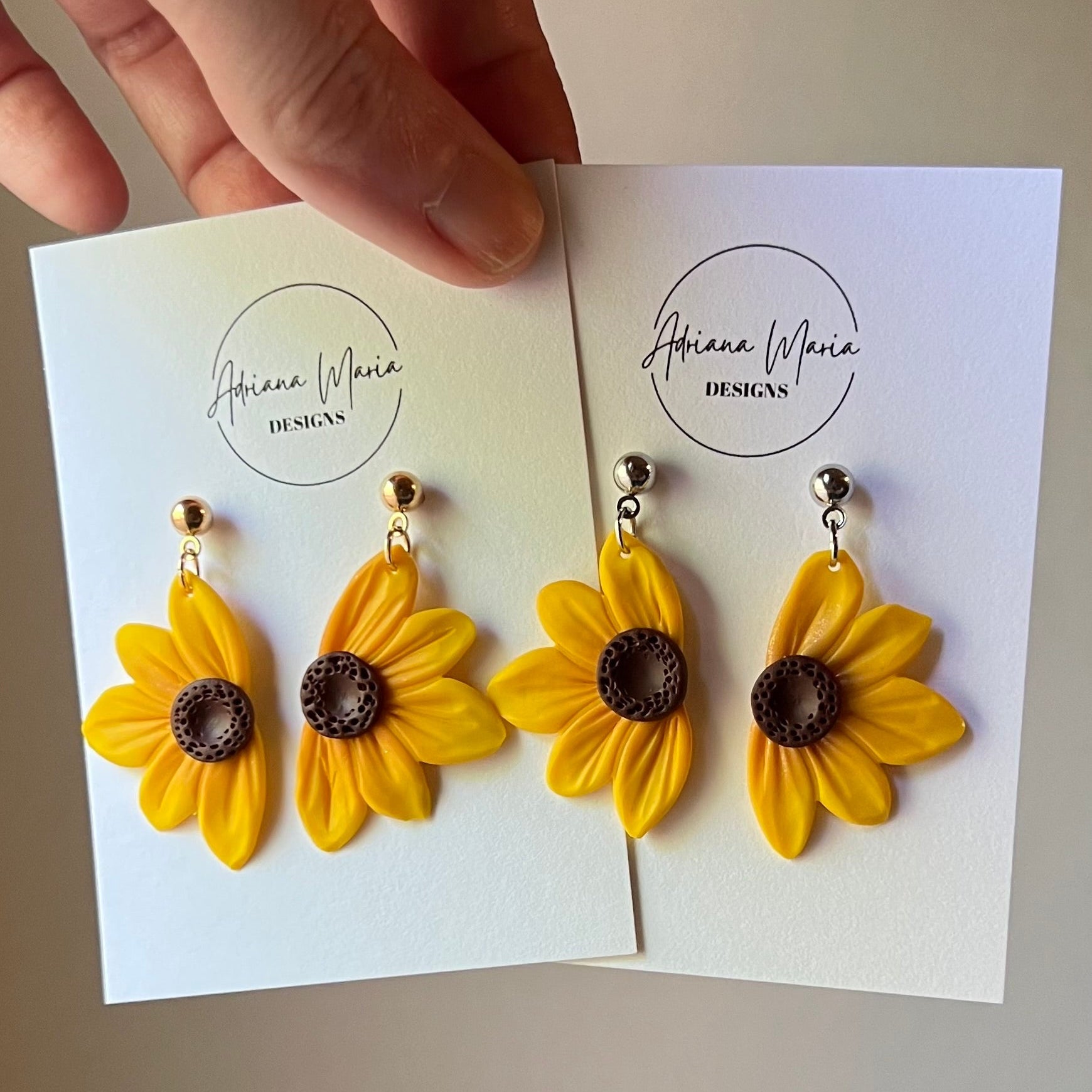 Yellow sunflower earrings on a branded card held by a hand.