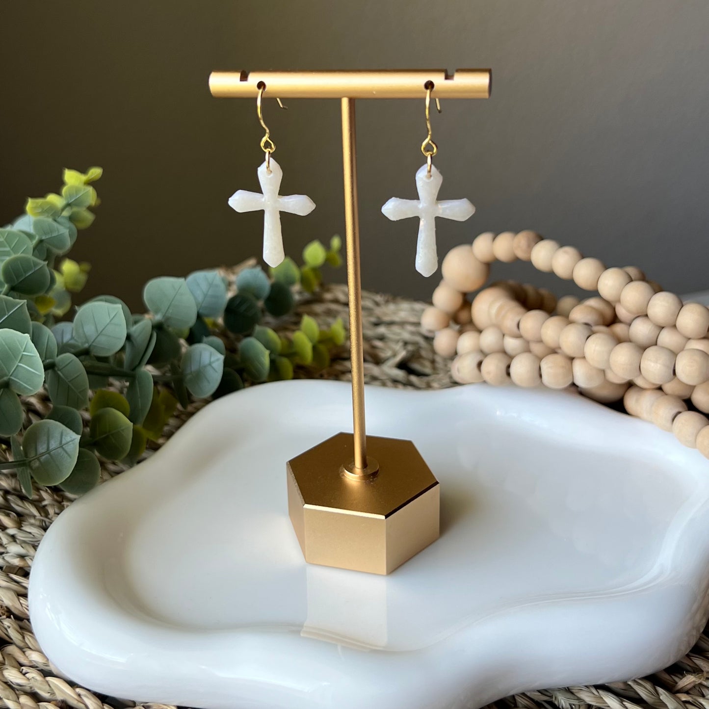 opal clay earrings shaped in crosses with gold plated stainless steel hooks hanging from earring stand 