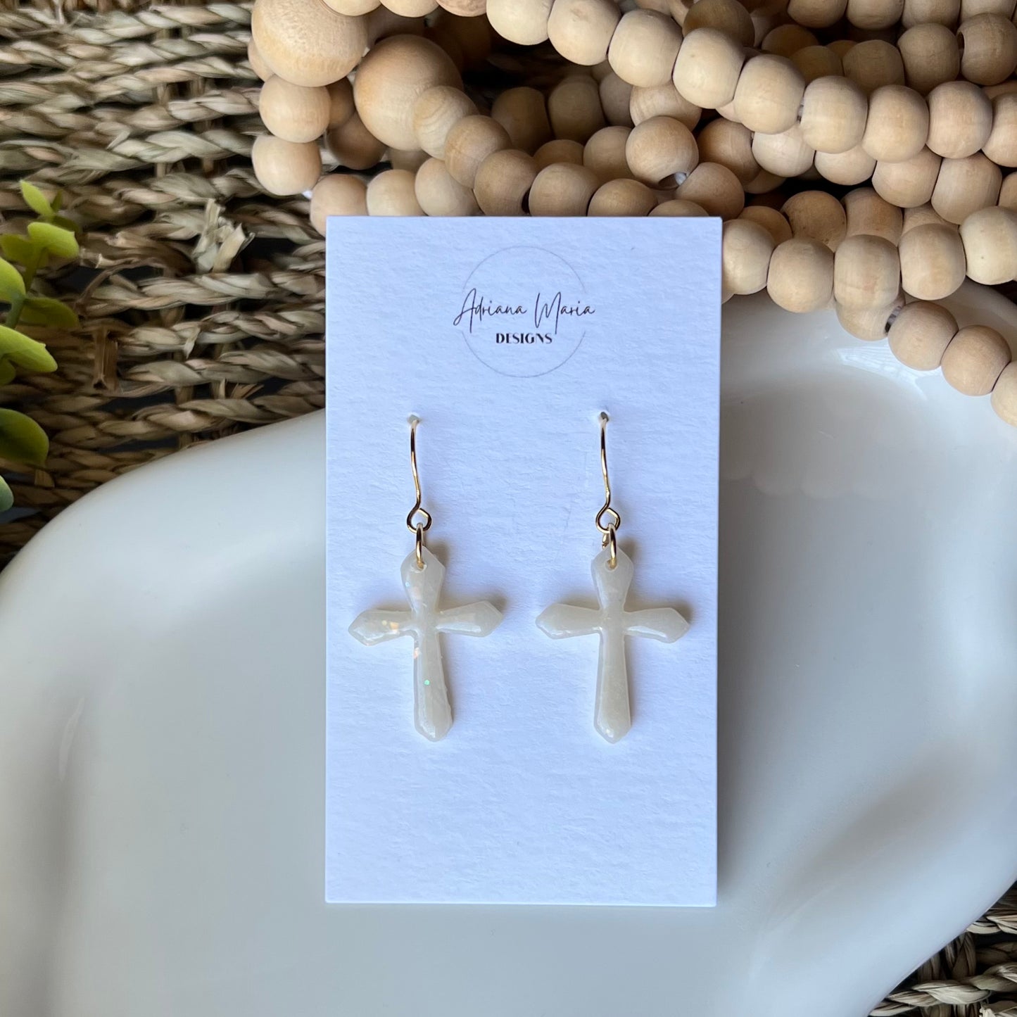 opal clay earrings shaped in crosses with gold plated stainless steel hooks. On a branded card sitting on a white plate 