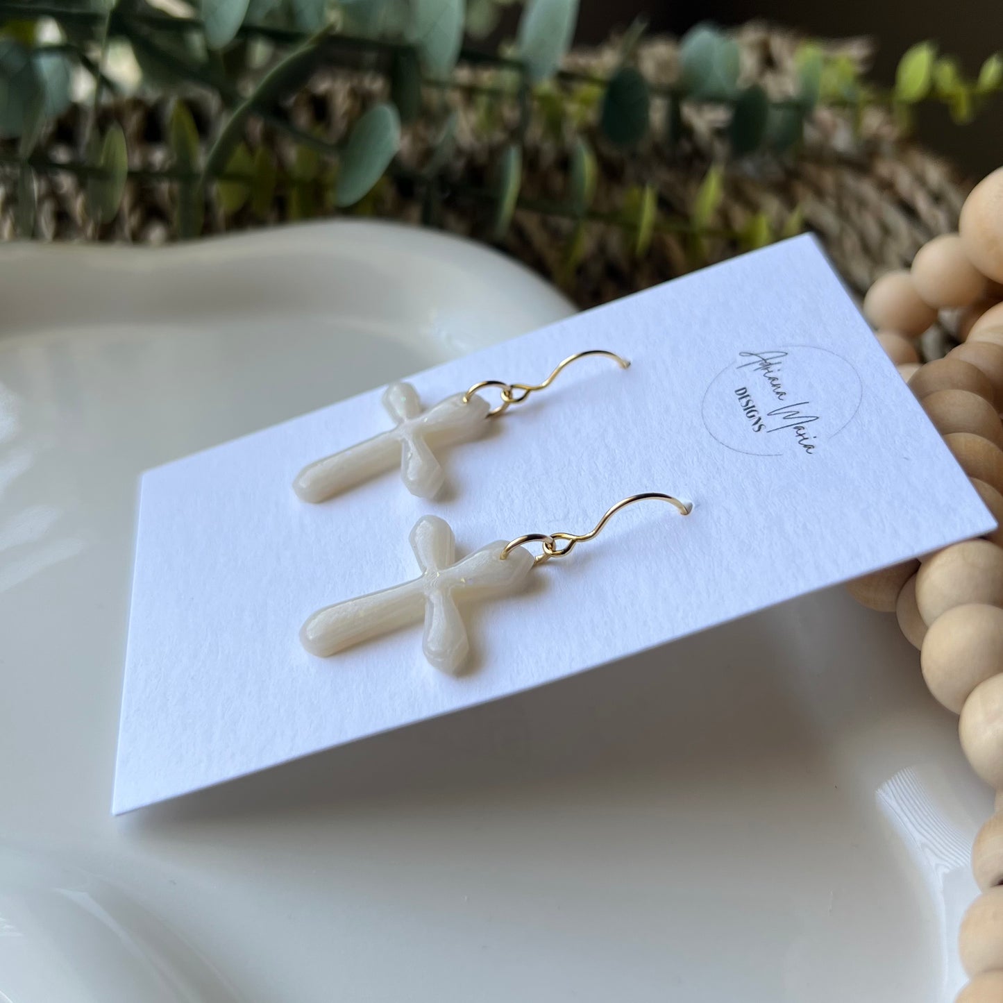 opal clay earrings shaped in crosses with gold plated stainless steel hooks. On a branded card sitting on a white plate 