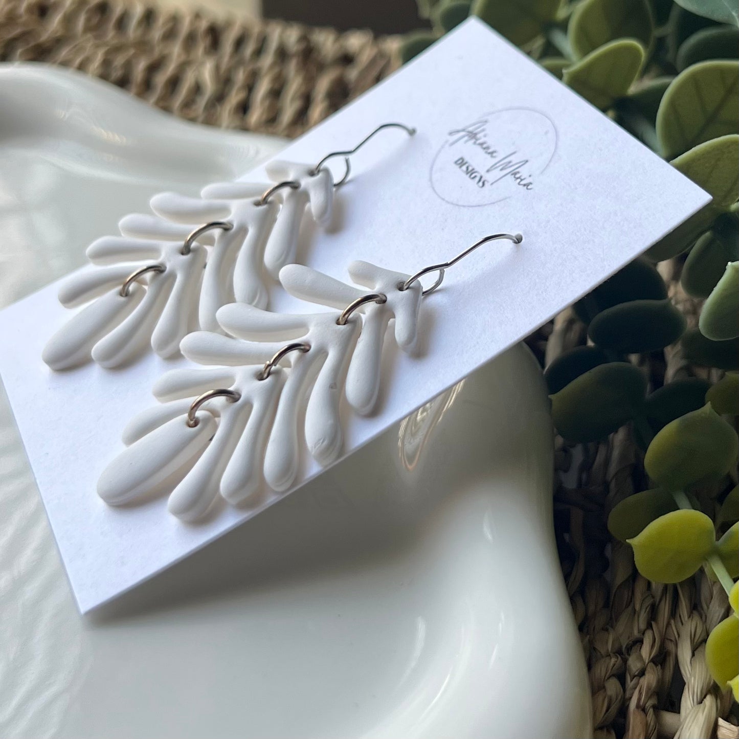 White leaf-shaped earrings with silver stainless steel hooks on a branded card with a natural background