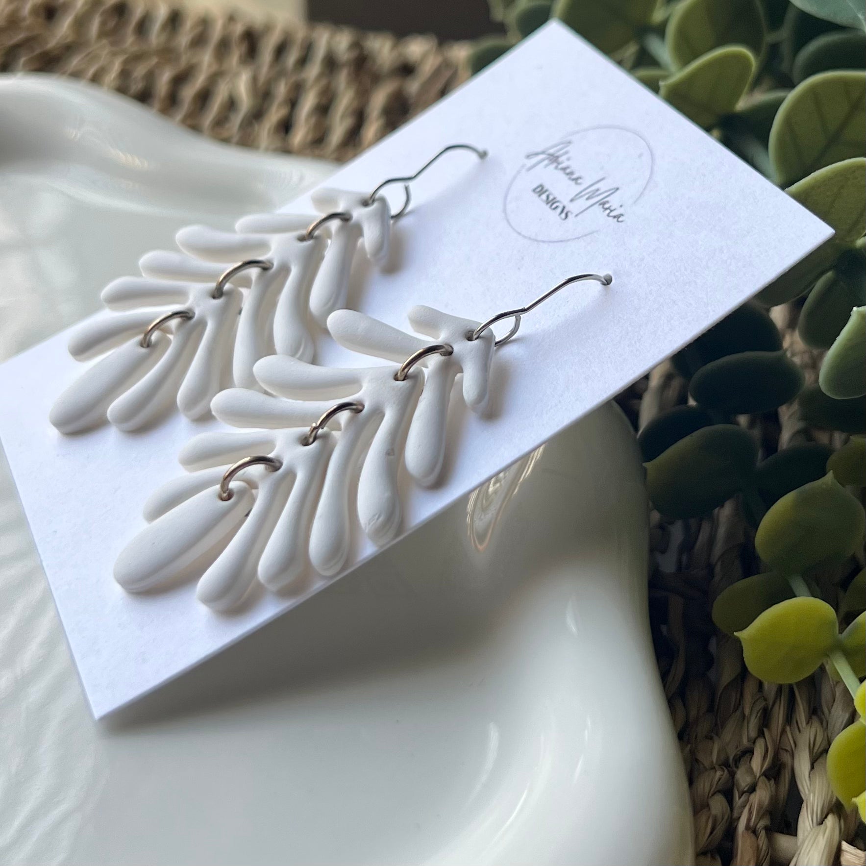 White leaf-shaped earrings with silver stainless steel hooks on a branded card with a natural background