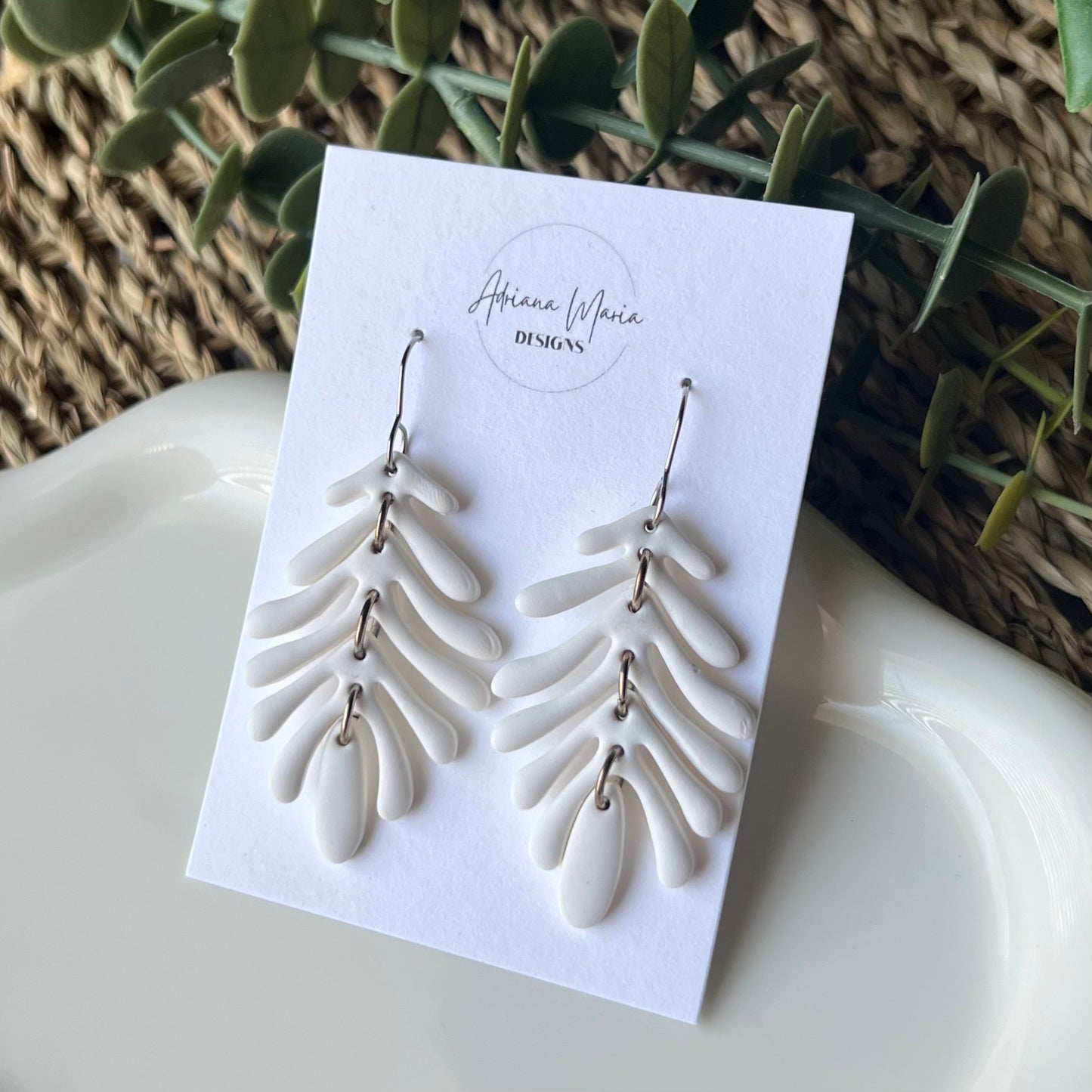 White leaf-shaped earrings with silver stainless steel hooks on a branded card with a natural background