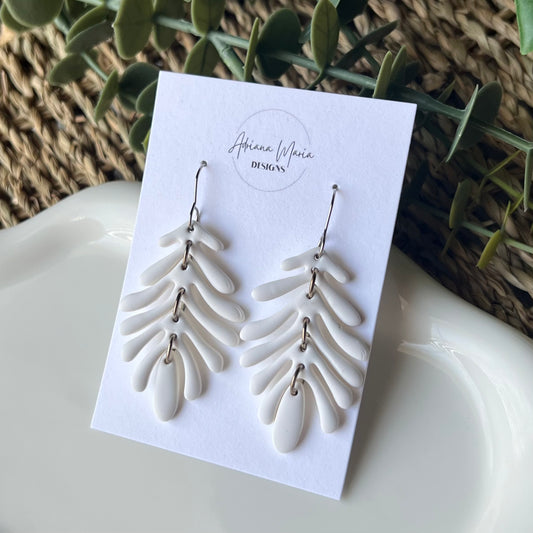 White leaf-shaped earrings with silver stainless steel hooks on a branded card with a natural background