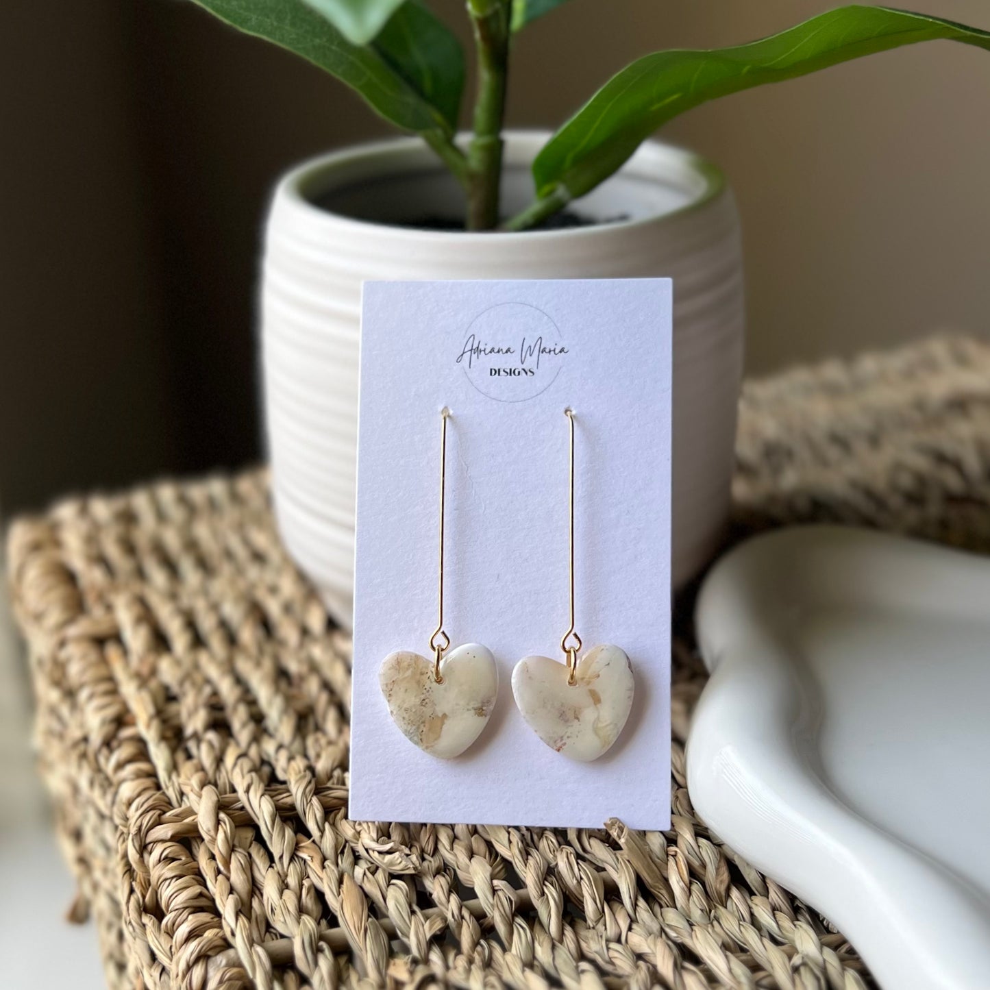 Heart-shaped earrings on a card with a plant and woven mat in the background
