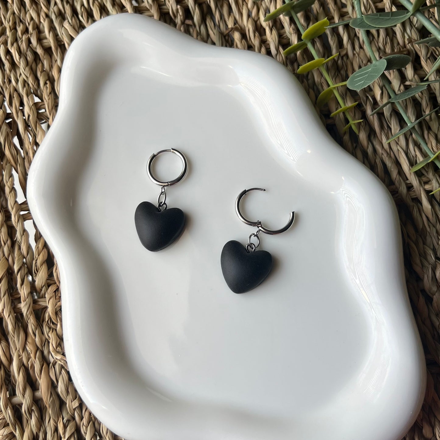 Black heart-shaped earrings on a white ceramic dish with a natural woven background